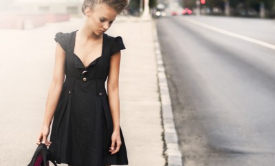 Woman wearing a little black dress walks down a road