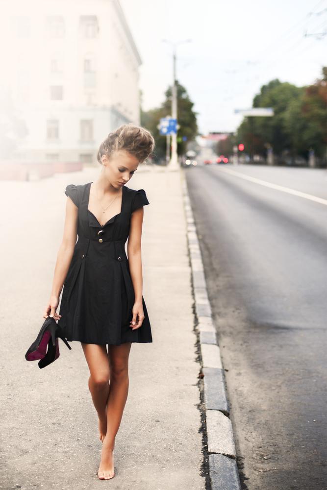 Woman wearing a little black dress walks down a road
