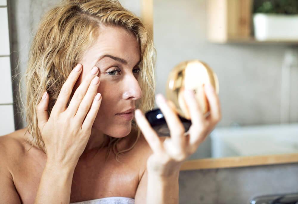 Woman examine her skin with a compact mirror