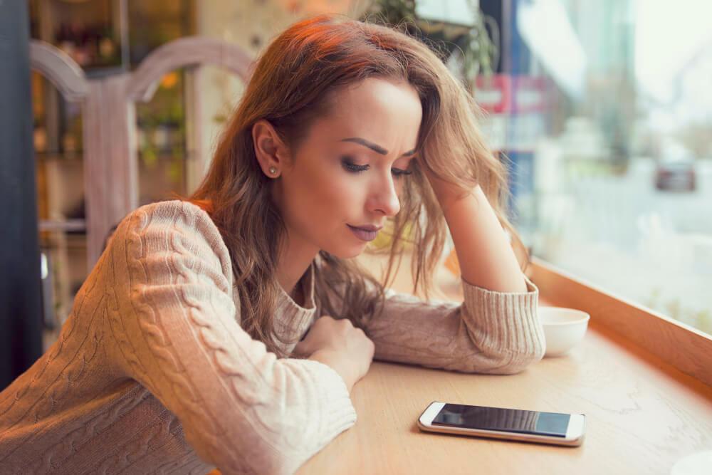 Unhappy woman staring at her phone in cafe