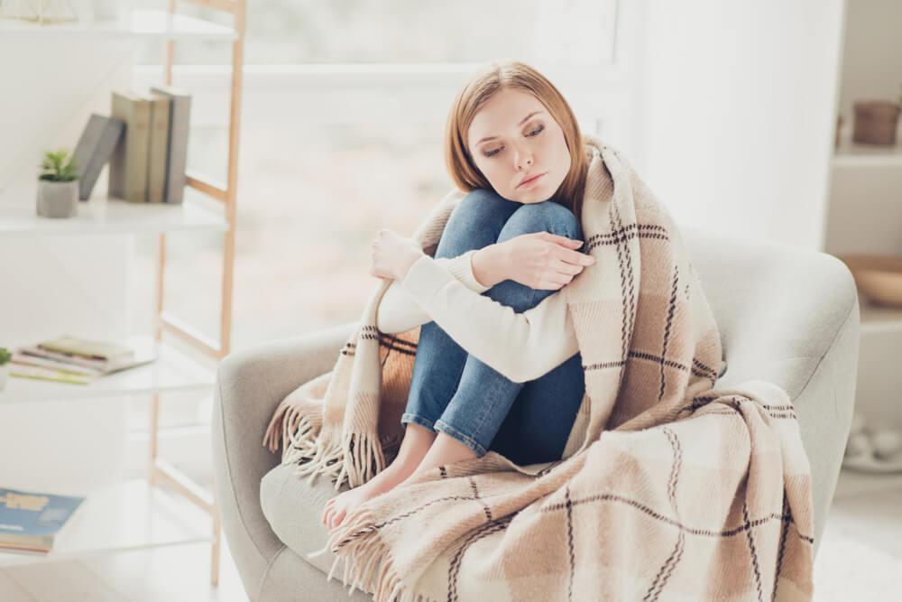 Woman hugging knees under blanket looking sad