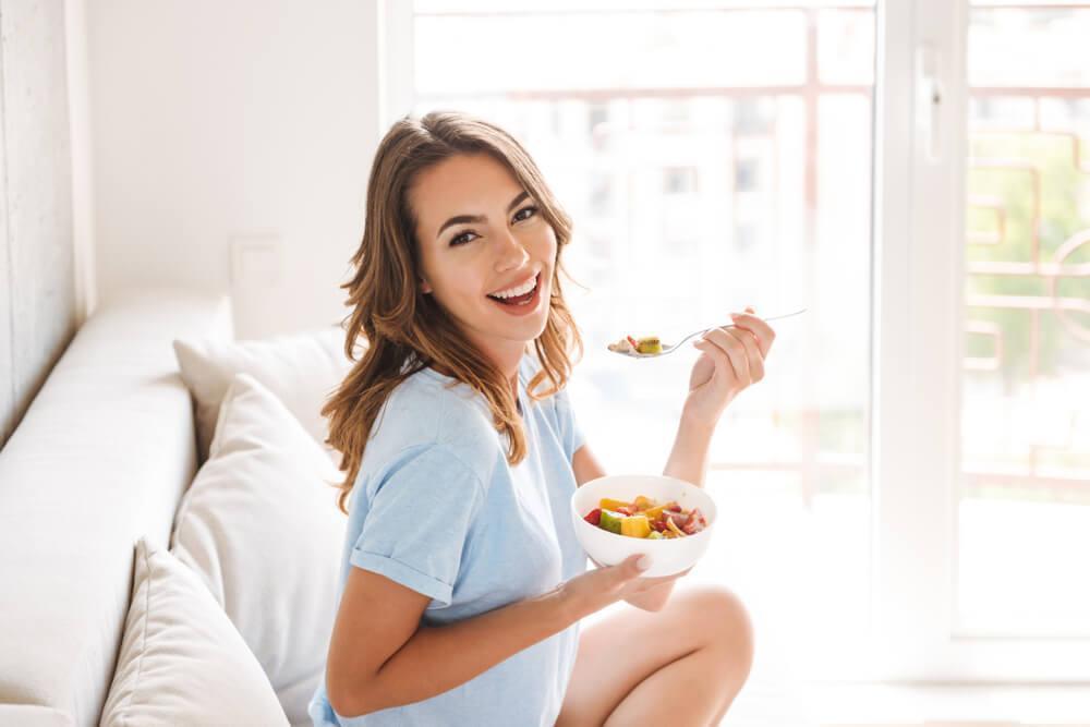 Woman on sofa eating fruit in bowl