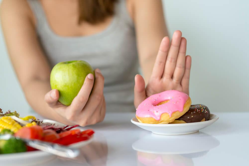 Woman's hand holding apple with other hand saying no to donut