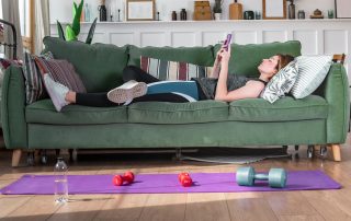 Woman lying on sofa looking at phone with no motivation to work out
